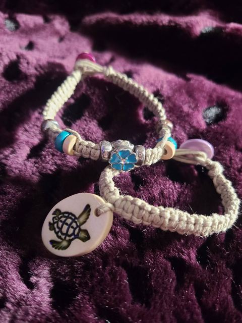 Two hemp bracelets, one with a blue flower charm and one with a turtle disc
