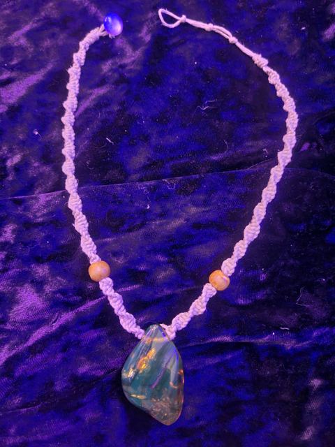 The finished twisted hemp necklace with two wood beads and a large polished stone pendant, under purple light